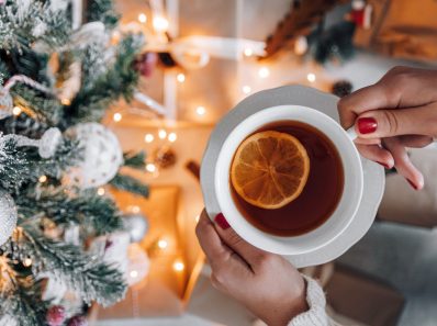 crop unrecognizable woman holding cup of tea near christmas tree